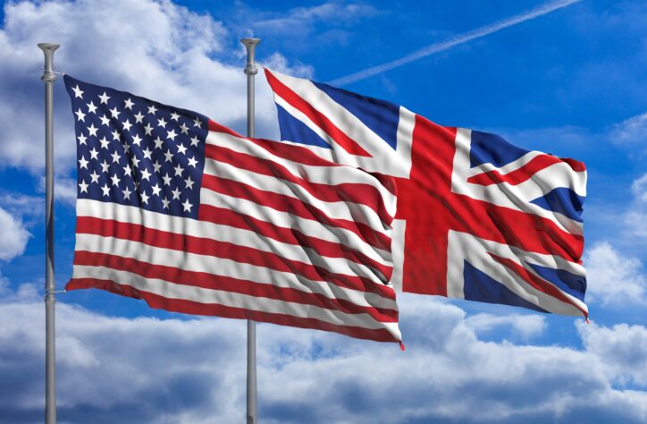 An Image of the UK and United States flags flying in front of a blue sky.