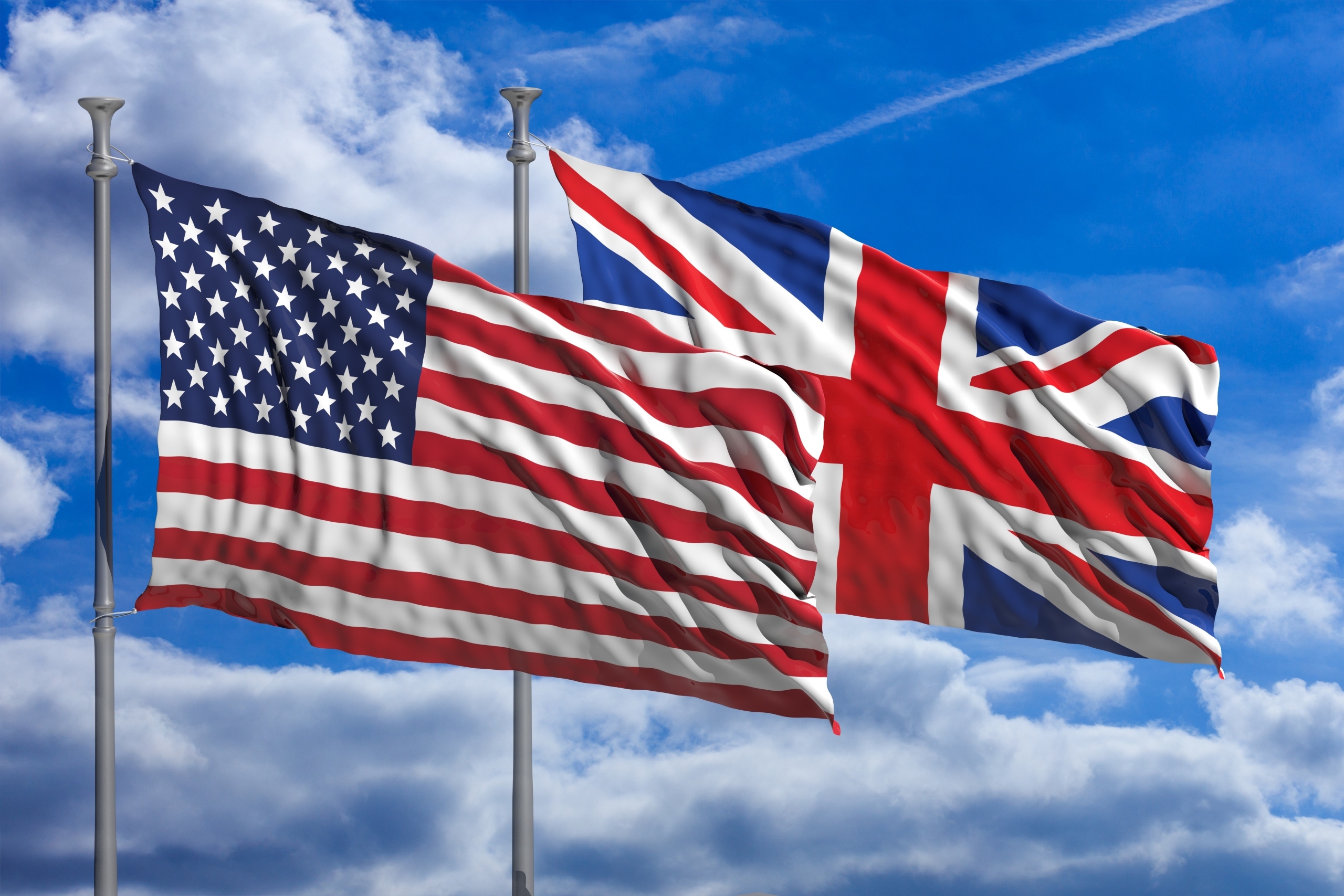 An Image of the UK and United States flags flying in front of a blue sky.